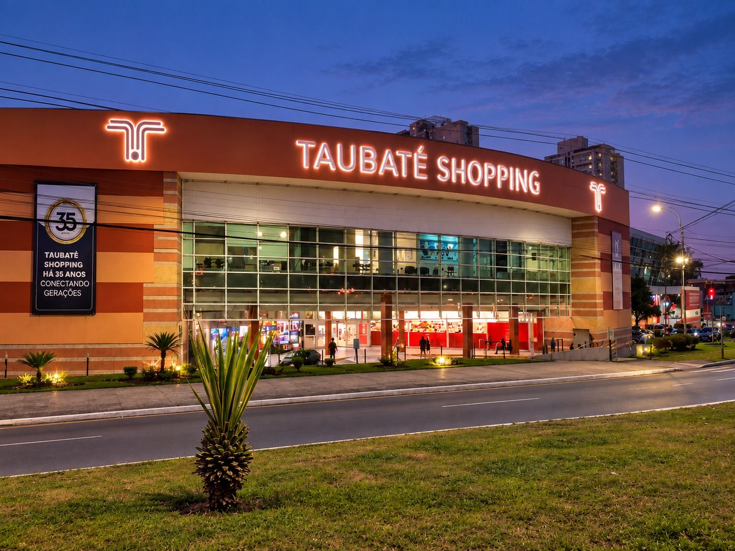Fachada do Taubaté Shopping ao entardecer com o letreiro iluminado em letras caixa